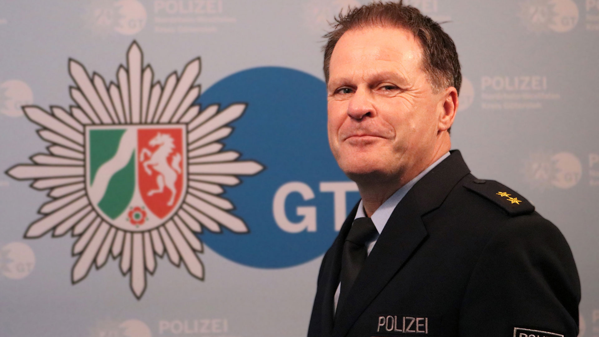 Volker Pfeiffer im Hintergrund das Logo der Polizei Gütersloh