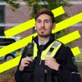 Portraitfoto von Polizeikommissar Justus. Hinter ihm ein grafisches Element. Drei neongelbe Querbalken. Im Hintergrund ein Streifenwagen, der vor einem Gebäude am Straßenrand parkt.