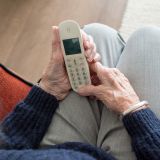 Blick von oben auf die Hände einer alten Person, die den Hörer eines kabellosen Telefon halten