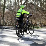 Ein Polizeibeamter in Fahrradkleidung schiebt ein Fahrrad über einen Zebrastreifen