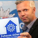 Uwe Arlitt und Guido Baratella halten die Zuhause sicher Plakette in die Kamera