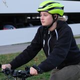 Eine junge Frau fährt Fahrrad. Sie trägt einen neonfarbenen Fahrradhelm. Im Ohr hat sie einen In-Ear Kopfhörer