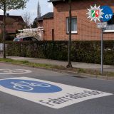 Eine Straße auf der groß auf der Fahrbahn das Verkehrszeichen Fahrradstraße aufgedruckt ist. Im Hintergrund sieht man zwei Radfahrende