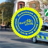 Im Vordergrund ist das Radschlag Logo zu sehen, daneben steht "für alle". Im Hintergrund, unscharf, ein Streifenwagen