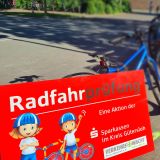 Schild mit der Aufschrift Radfahrprüfung. Dahinter, unscharf, ein blaues Kinderfahrrad