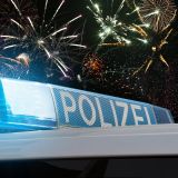 Zu sehen ist das Blaulicht eines Streifenwagens mit der Aufschrift Polizei. Im Hintergrund sieht man einen nächtlichen Himmel mit Feuerwerk