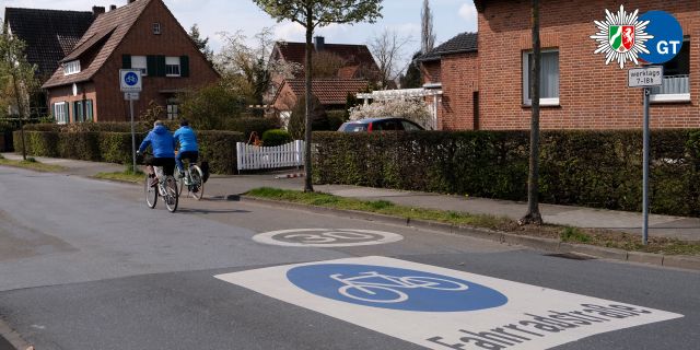 Eine Straße auf der groß auf der Fahrbahn das Verkehrszeichen Fahrradstraße aufgedruckt ist. Im Hintergrund sieht man zwei Radfahrende