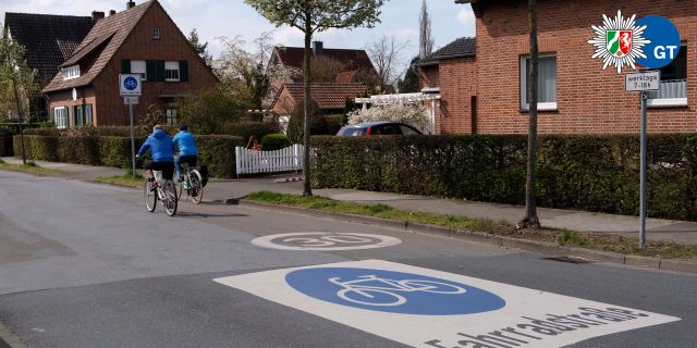 Eine Straße auf der groß auf der Fahrbahn das Verkehrszeichen Fahrradstraße aufgedruckt ist. Im Hintergrund sieht man zwei Radfahrende