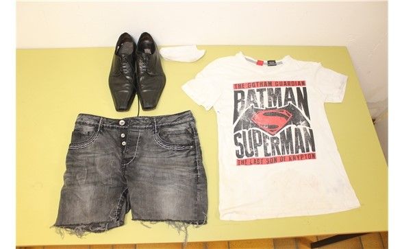 Drei Kleidungsstücke: schwarze Lederschuhe, eine grau verwaschene Shorts, ein weißes T-Shirt mit der Aufschrift Batman Superman und dem Superman Logo 