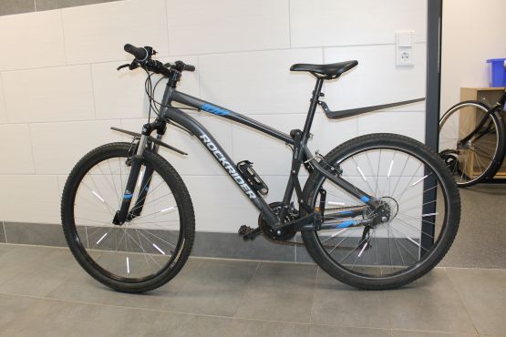 graues Mountainbike, Rockrider, Modell 100, mit silbernem und blauem Aufdruck auf dem Rahmen